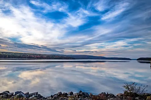 The Quabbin Reservoir at dusk, still water reflecting a wide streaked sky with a low wooded shoreline in the distance.